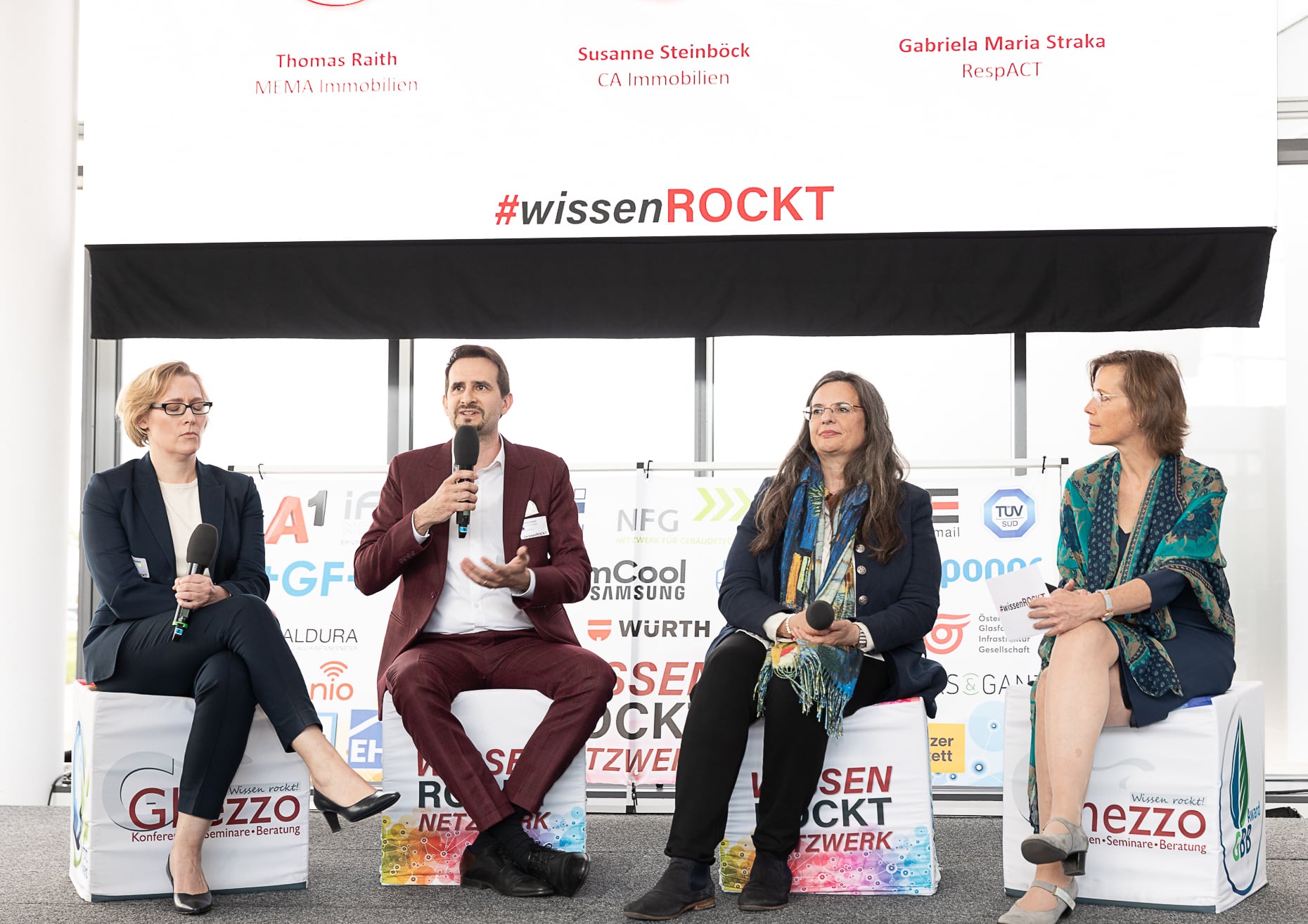 Podium mit vier Teilnehmenden vor #wissenROCKT-Banner beim 7. Ghezzo Immobilientag